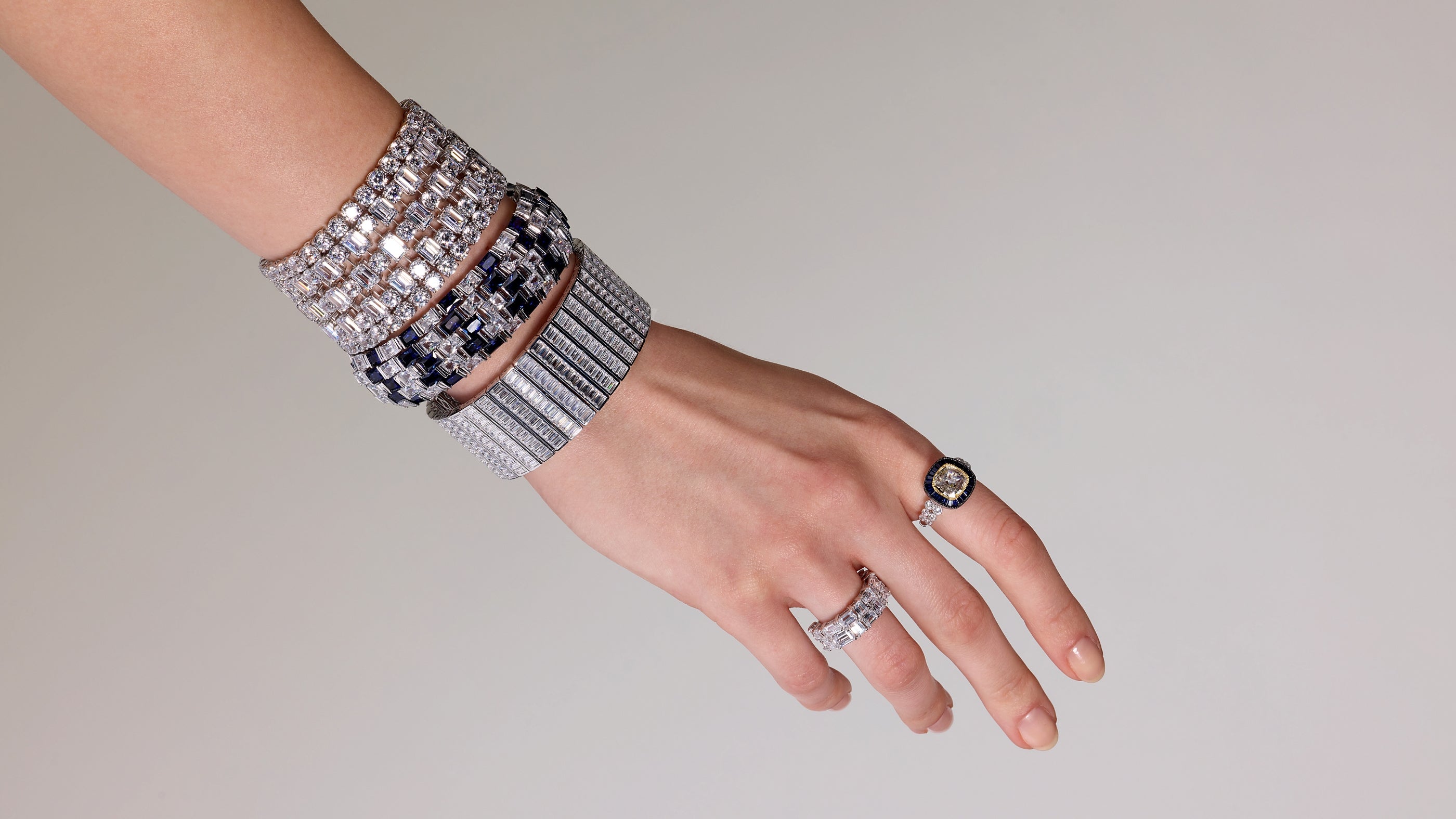 Hand elegantly stacking bracelets, tennis bracelets, and rings for a stylish, layered jewelry look.